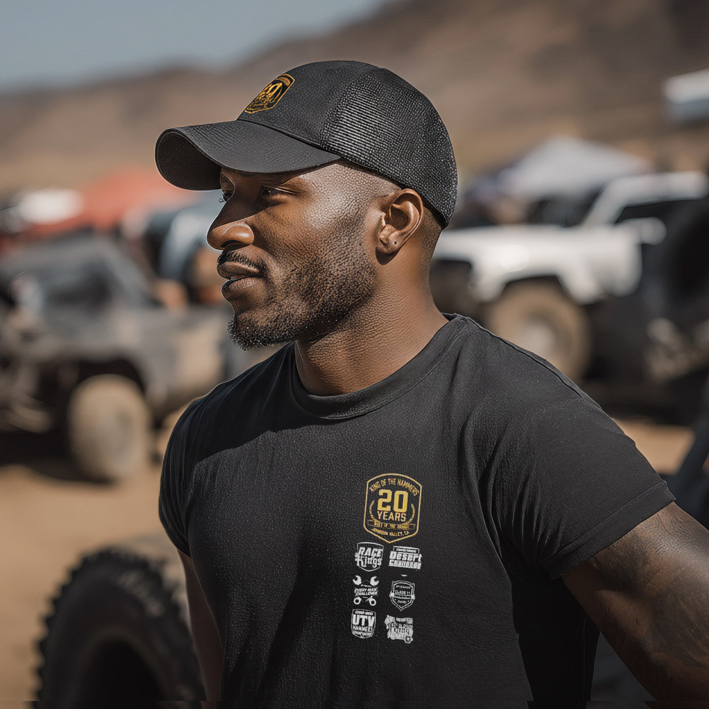 Man wearing a black King of the Hammers cap and t-shirt with vehicle logos in an off-road setting