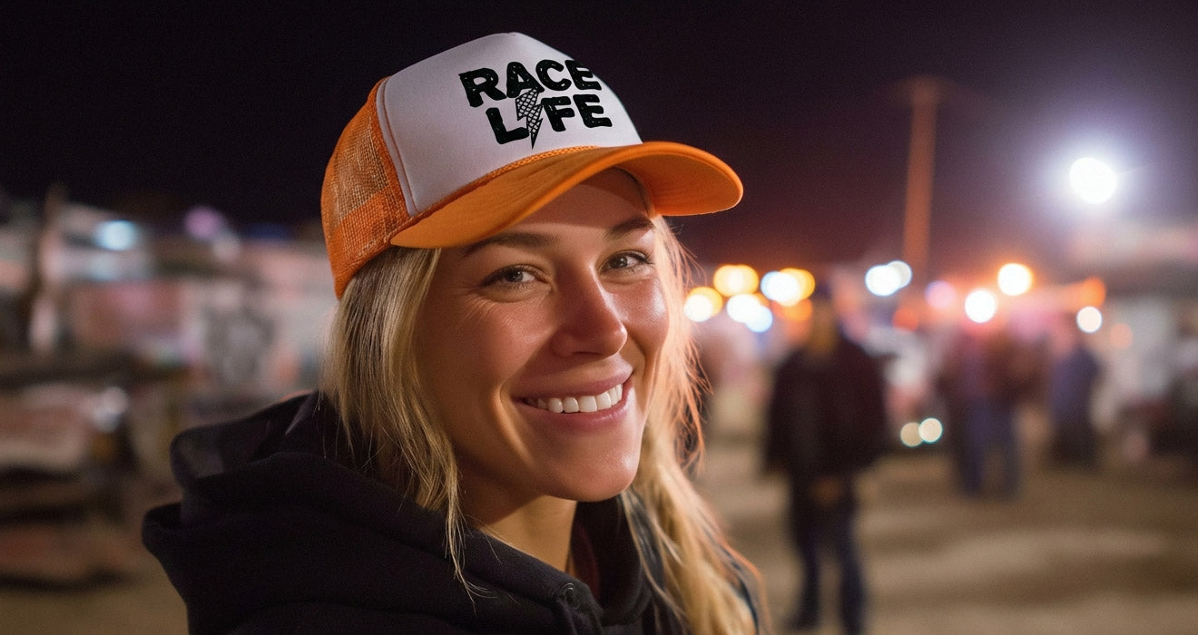Smiling woman wearing an orange and white cap with 'Race for Life' text at a nighttime event.